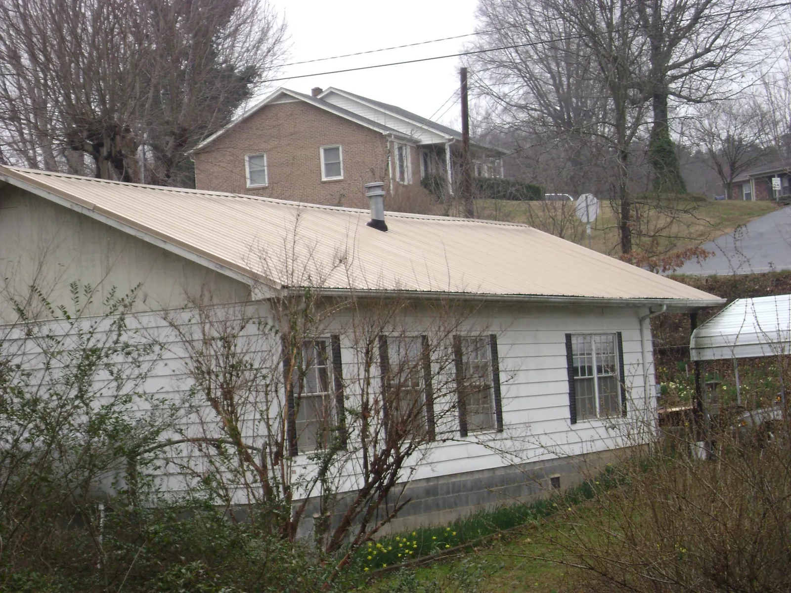 Tan metal roof on a white sided house set into a hillside — Commercial Roofing by Roofing Brothers in Youngstown